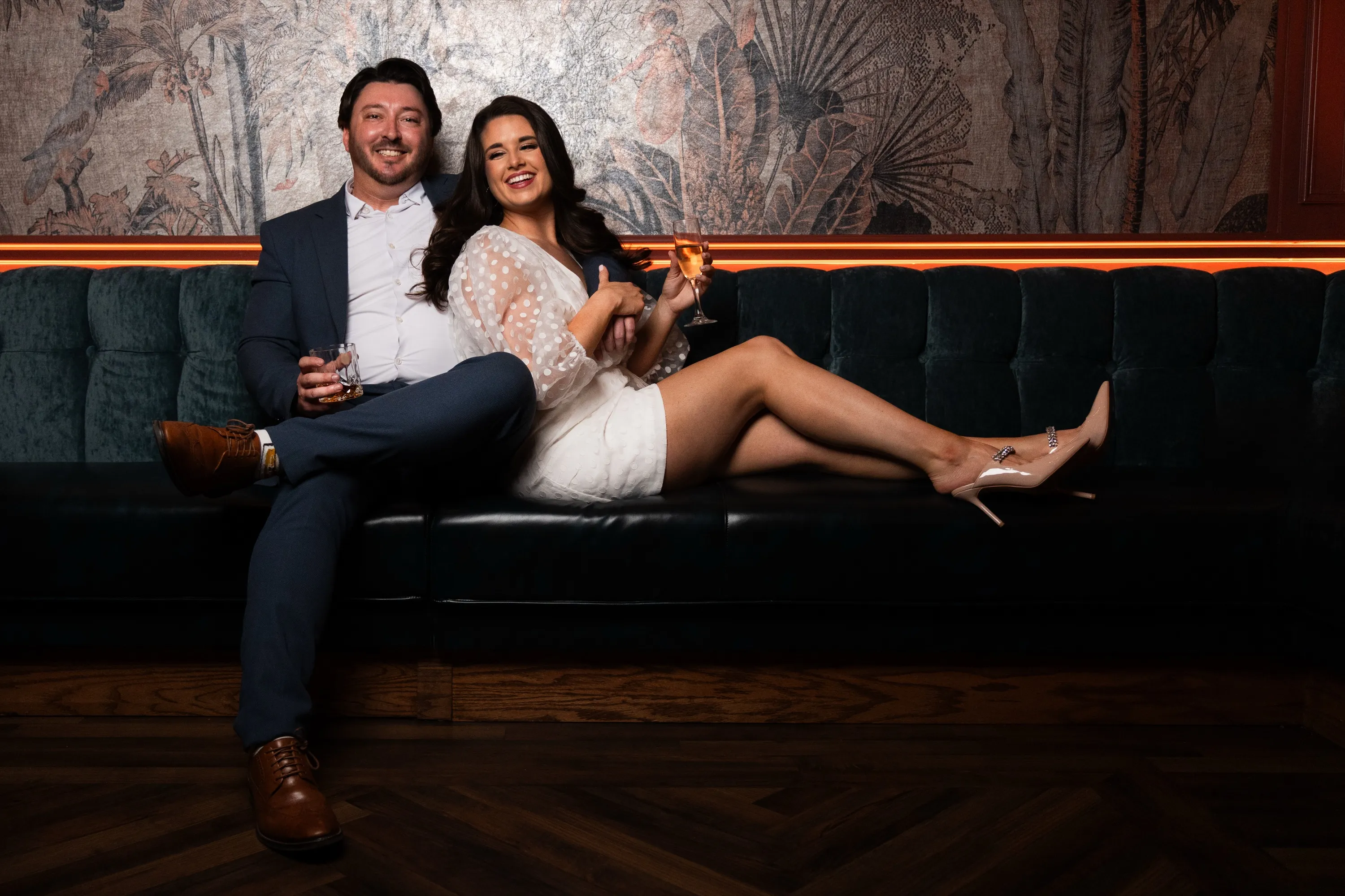 Pareja comprometida riendo en un sillón de terciopelo del bar durante su sesión de compromiso en Columbian Country Club