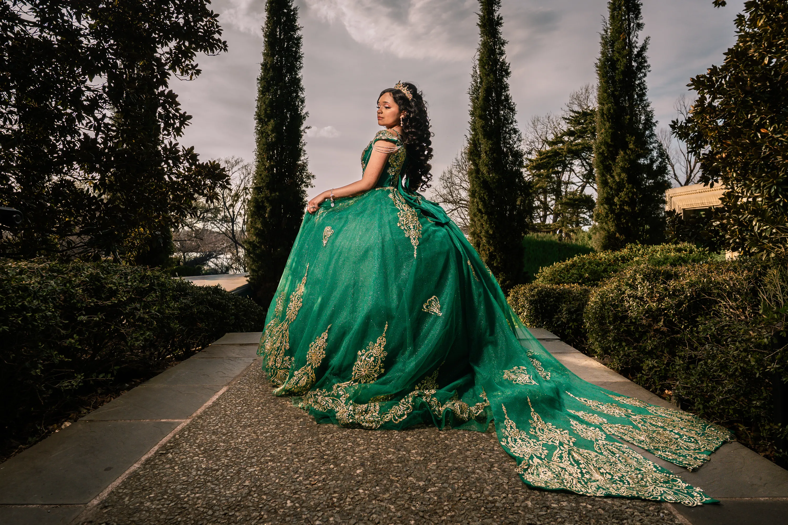 Quinceañera in an emerald and gold quince gown on a garden walkway at the Dallas Arboretum