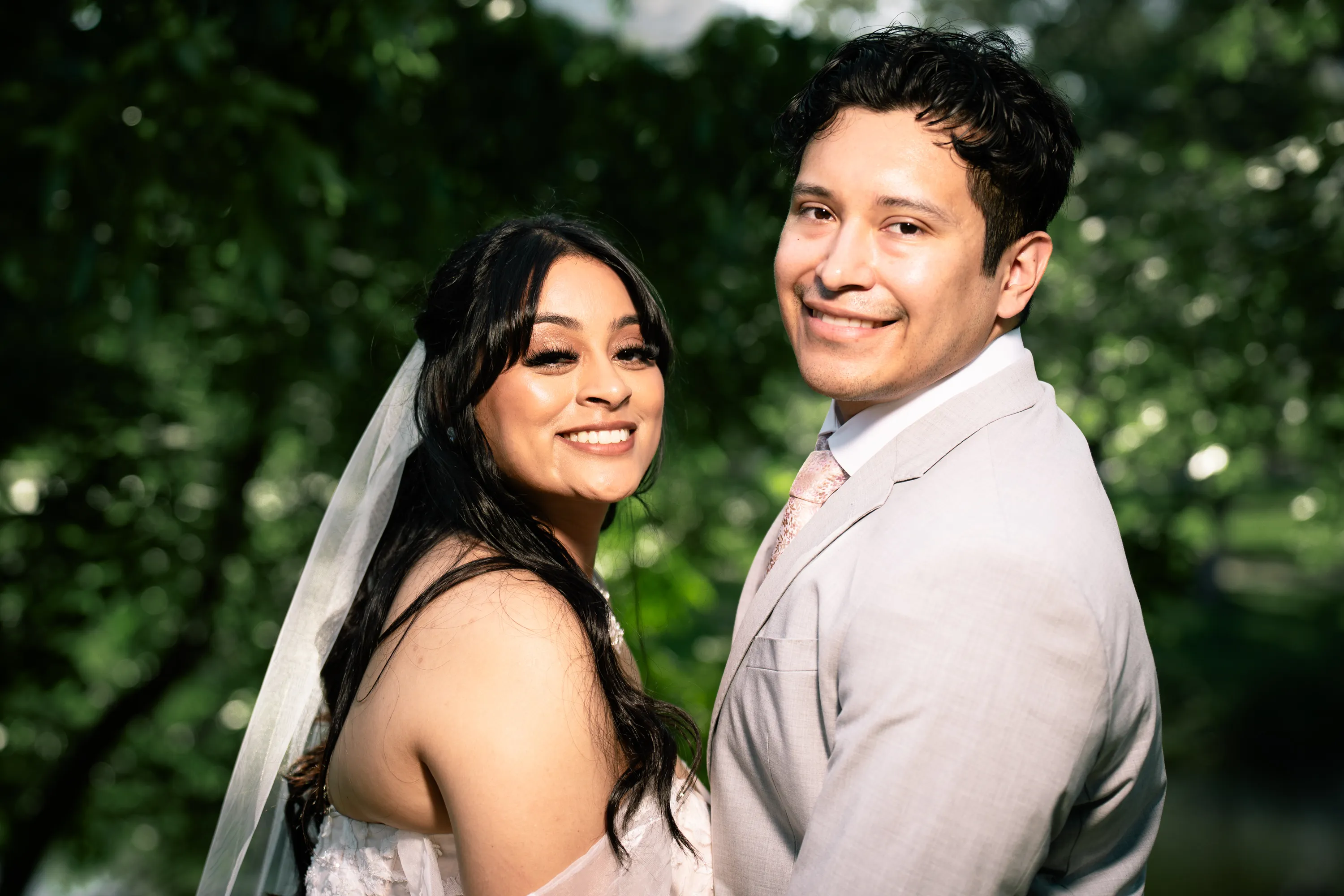 Retrato de los novios sonriendo entre los árboles de Turtle Creek Park en Dallas