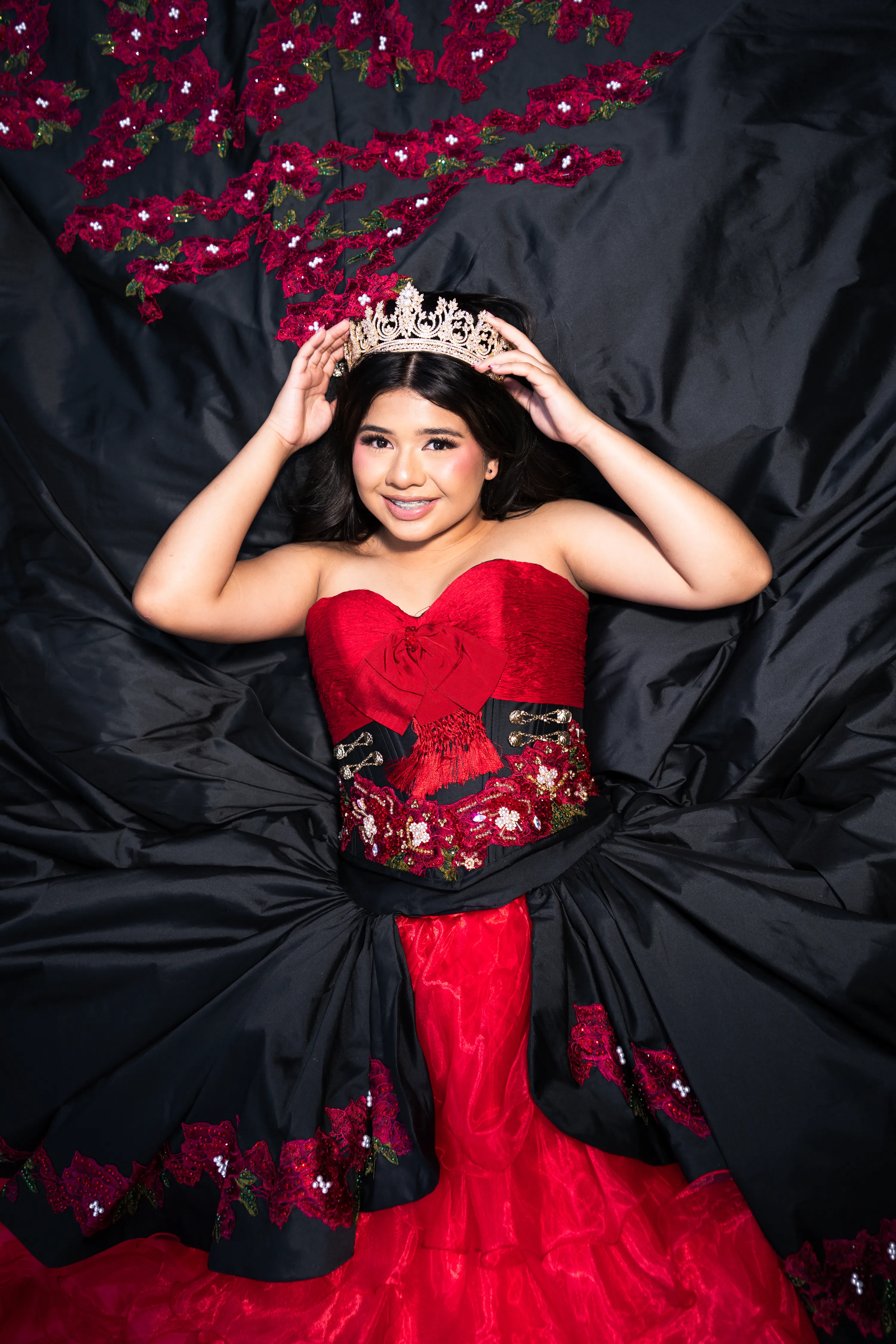 Quinceañera con vestido charro negro y rojo con rosas colocándose su corona dorada en el Mandalay Canal de Irving, Texas