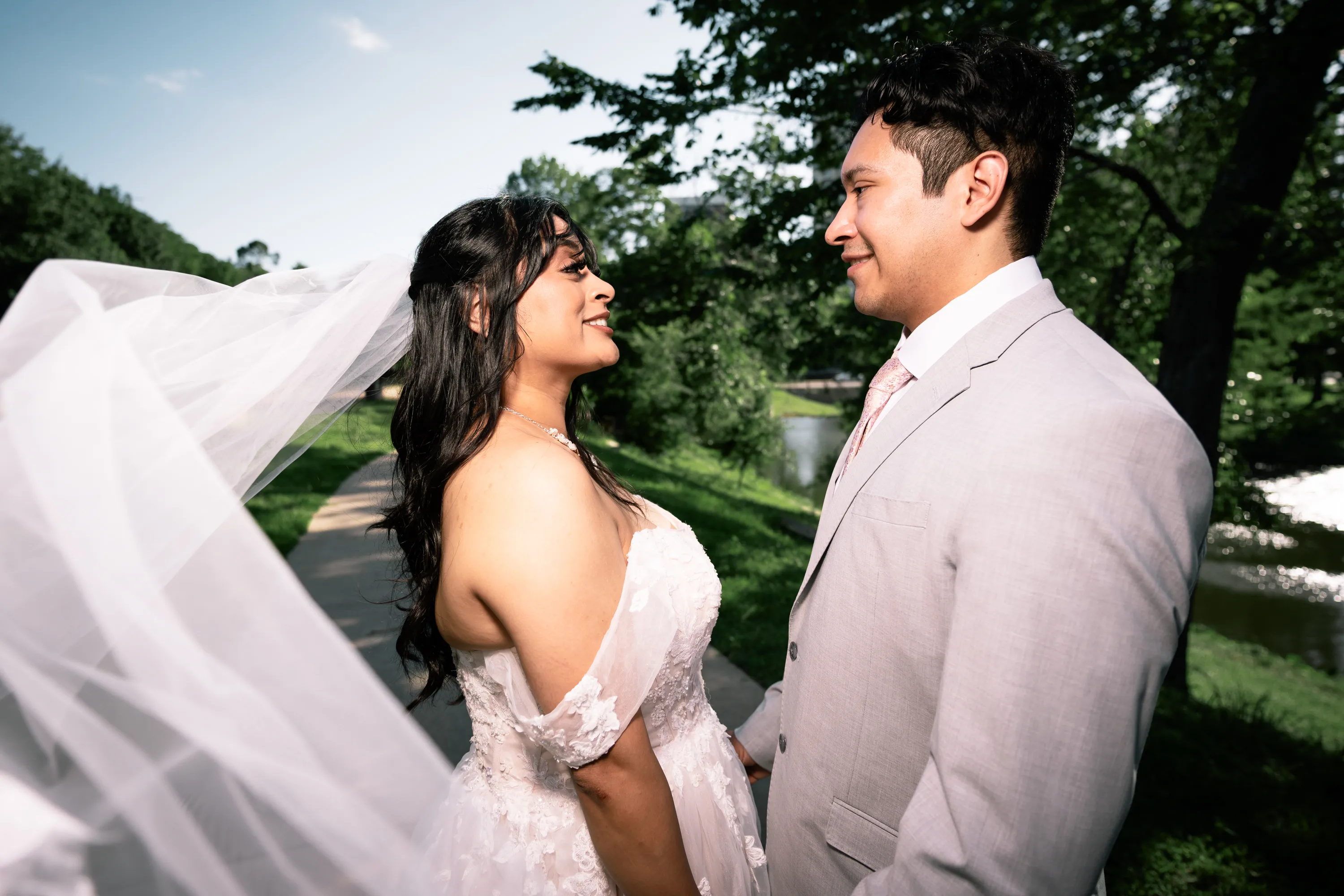Novia con el velo al viento sonriéndole a su novio en Turtle Creek Park en Dallas