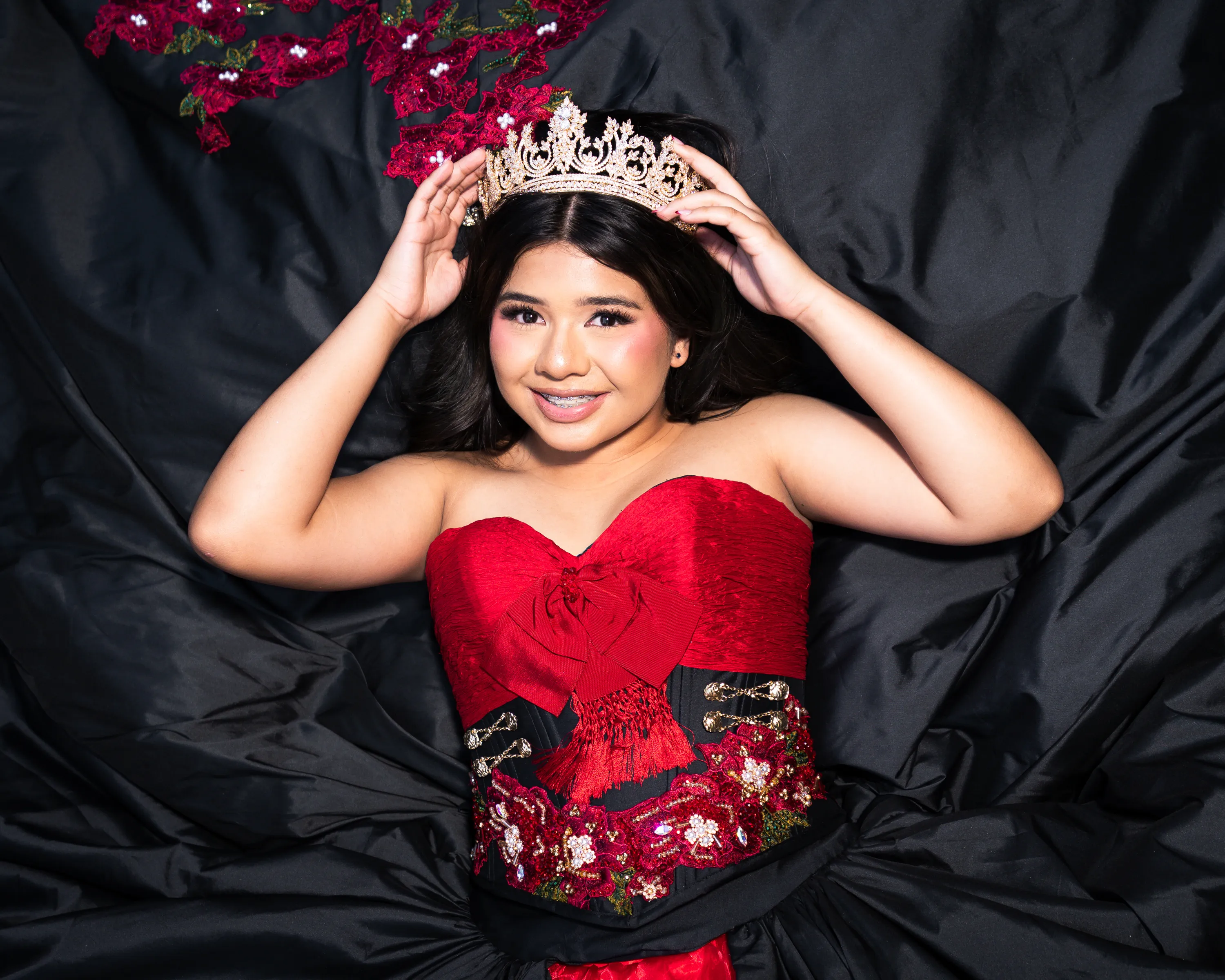 Quinceañera con vestido charro negro y rojo con rosas colocándose su corona dorada en el Mandalay Canal de Irving, Texas
