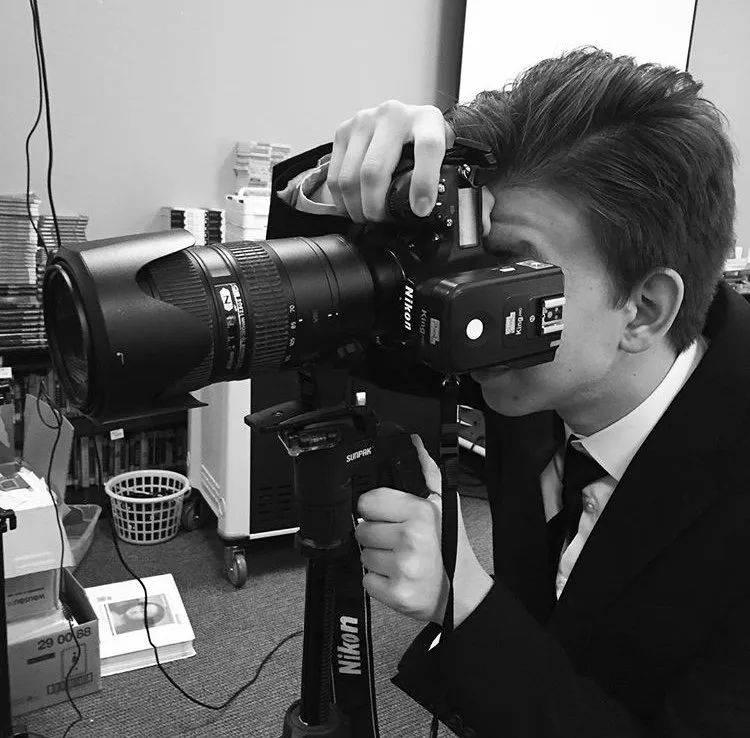 Un fotógrafo de bodas en Dallas, de traje, fotografiando a unos recién casados con una cámara profesional sobre un tripié en interiores.