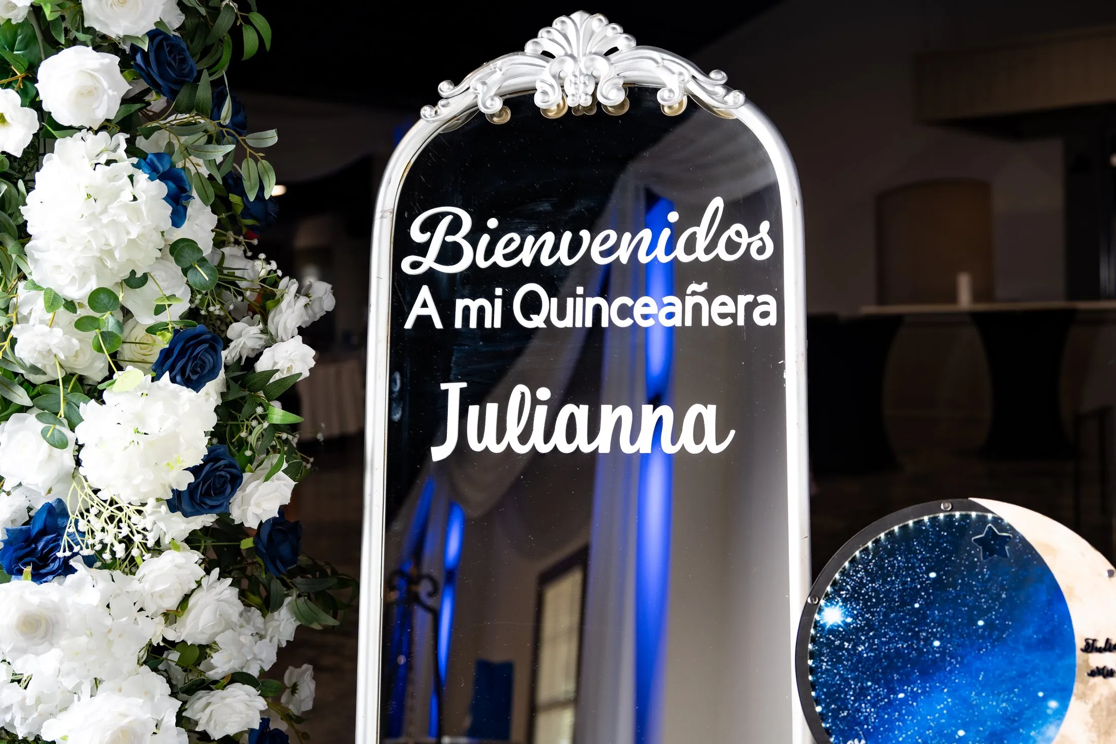 “Bienvenidos a mi Quinceañera” welcome sign framed by white and navy roses