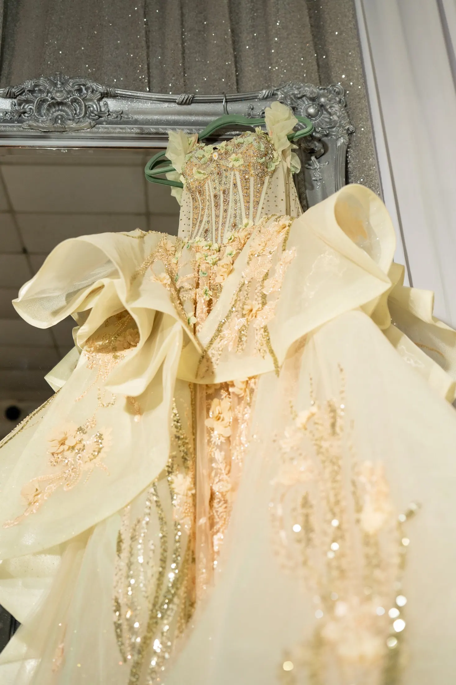 Champagne-gold Sweet 16 quince gown hanging by an ornate mirror