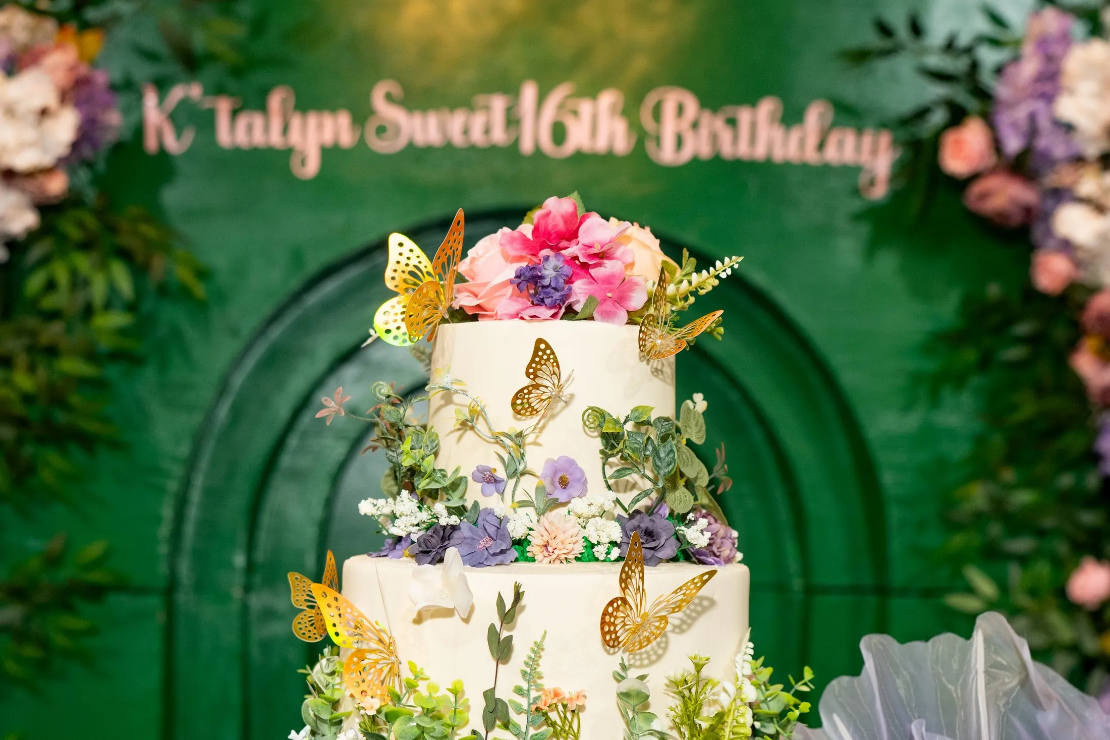 Enchanted garden Sweet 16 cake with butterflies in front of the green arch backdrop