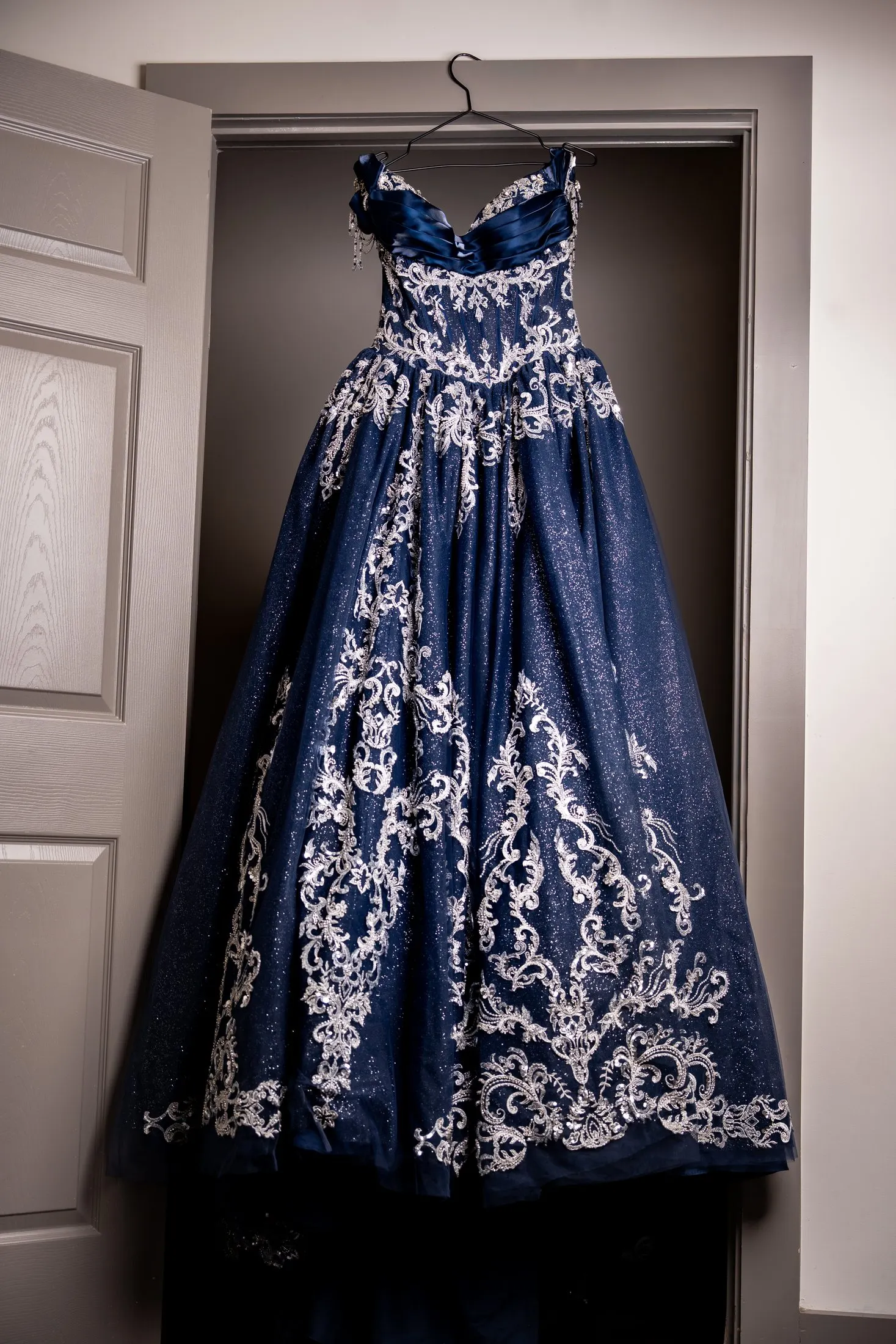 Navy blue and silver embroidered quinceañera dress hanging in a doorway