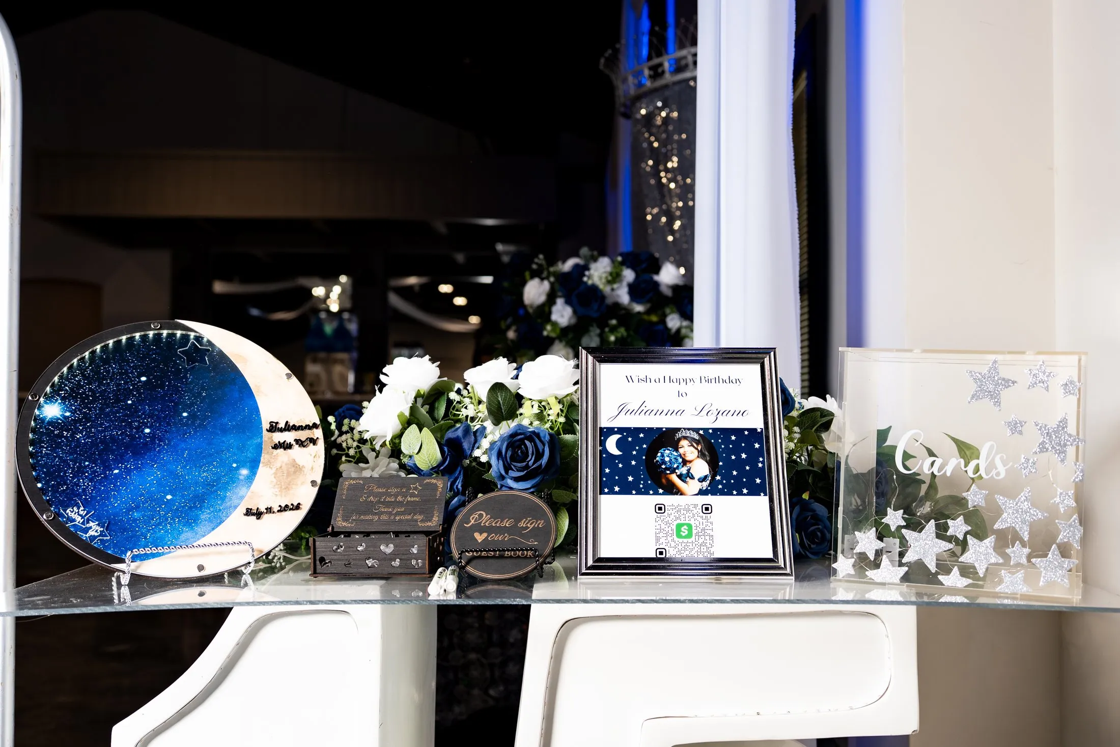 Navy and silver quinceañera welcome table with a starry moon guest book and white roses at Diamond Ranch Event Center in Waxahachie, Texas