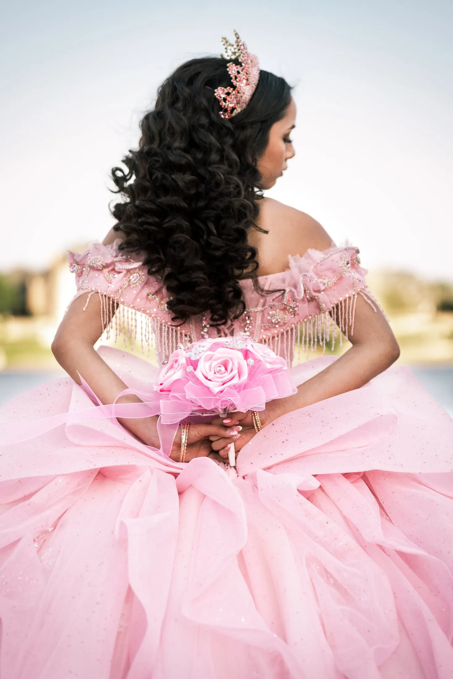 Back view of the pink quinceañera gown, curls and crown by the lake at Adriatica Village in McKinney, Texas