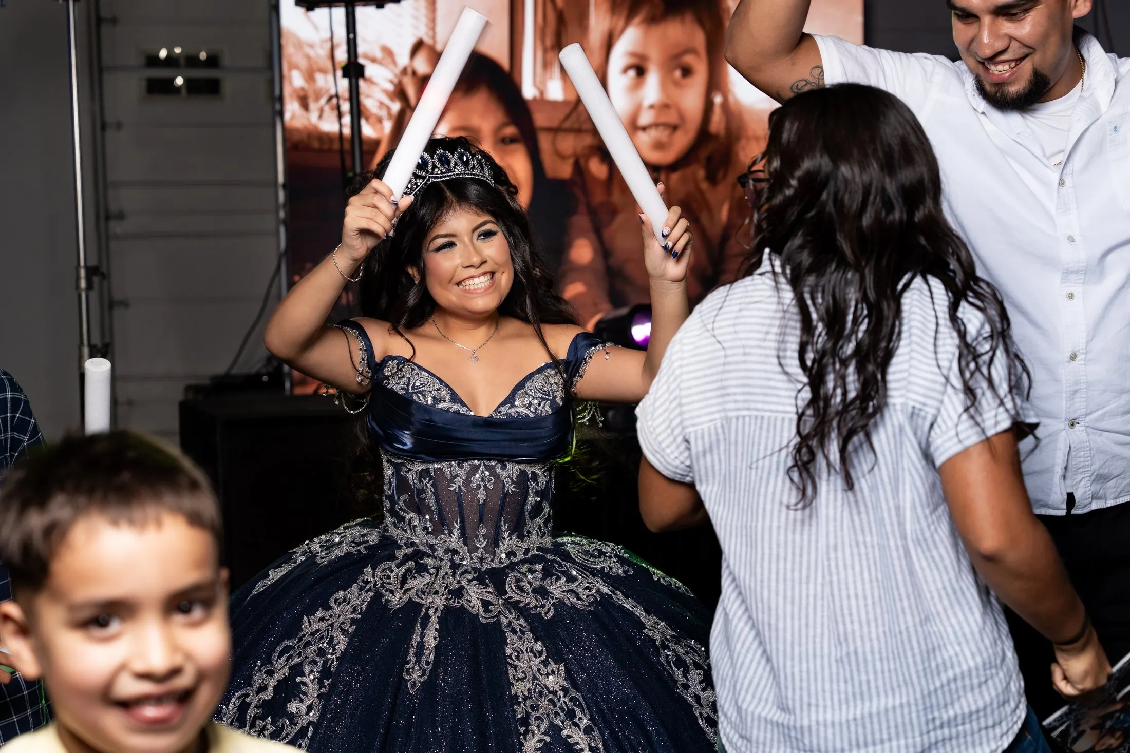 Quinceañera dancing with family and foam sticks, a little cousin smiling in front