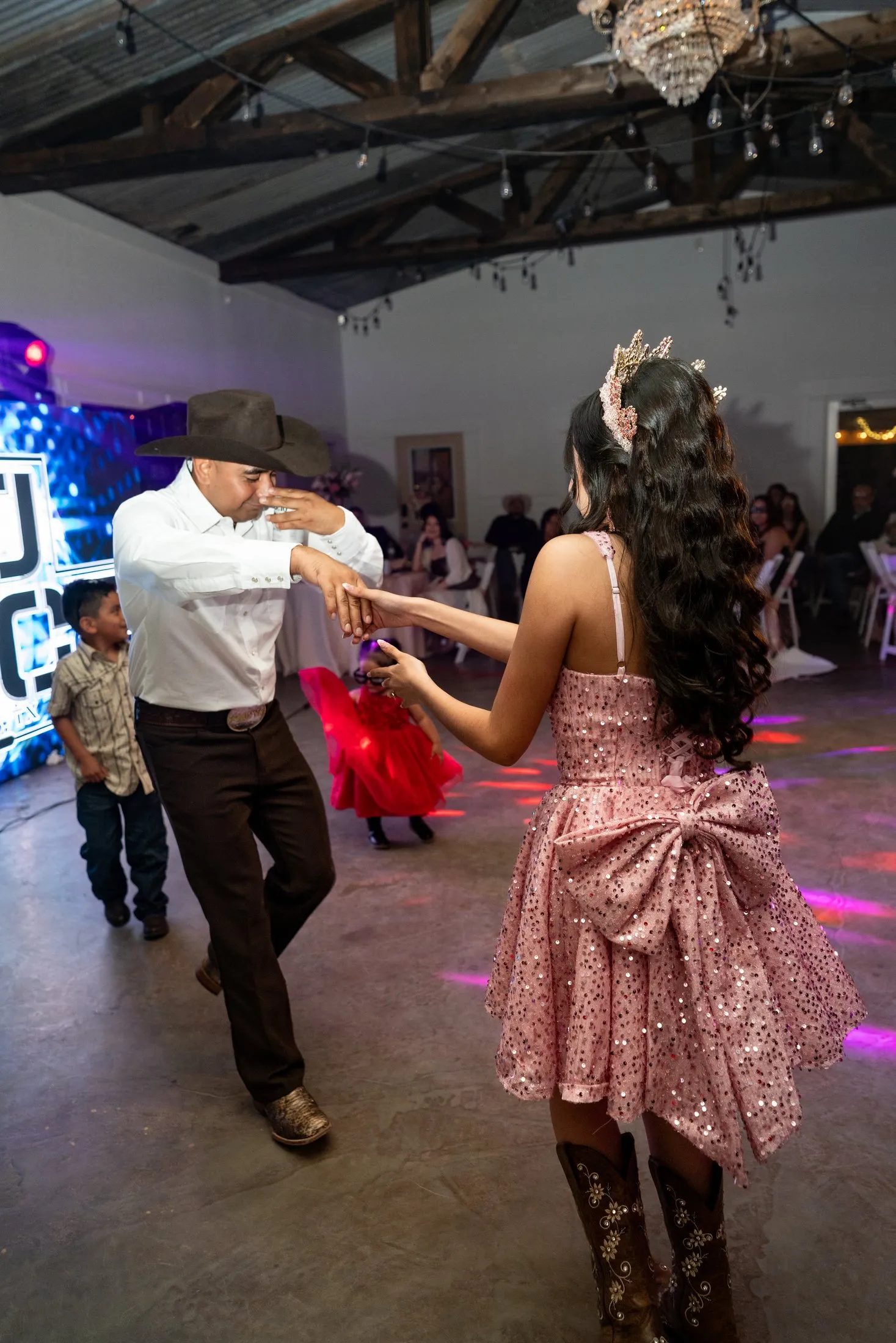 Quinceañera in her pink sequin dress and cowgirl boots dancing with a guest at Hidden Acres Ranch in Hudson Oaks