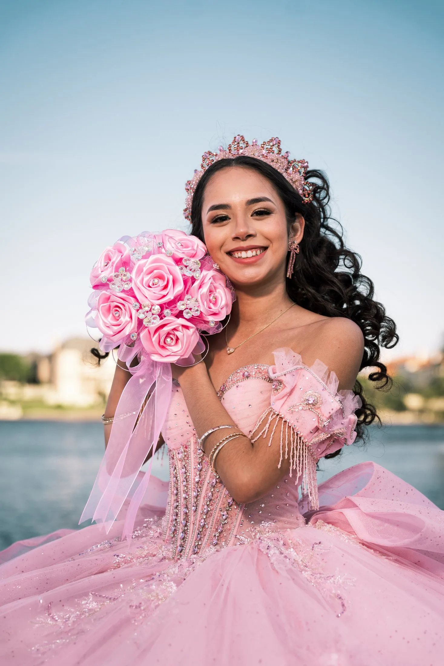 Smiling quinceañera holding a pink rose bouquet in her crown