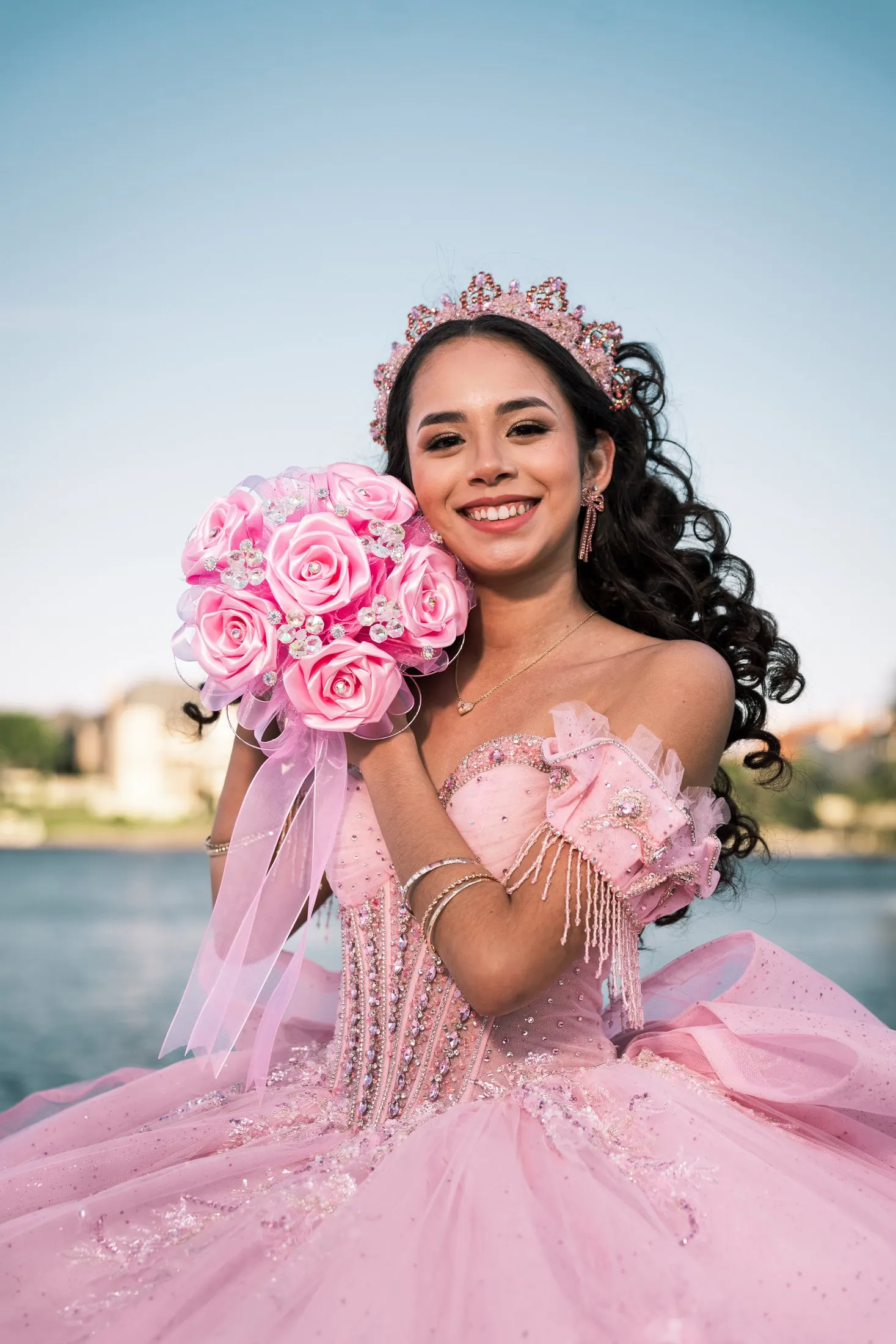 Smiling quinceañera holding a pink rose bouquet in her crown